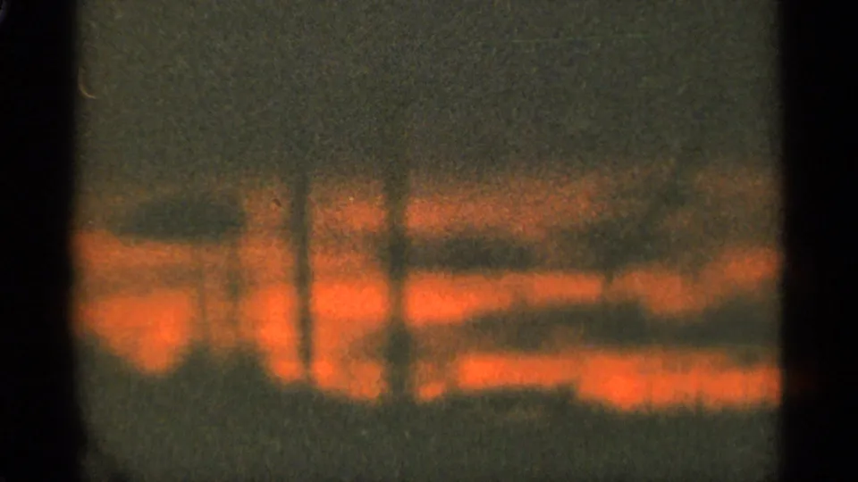 Abstract-looking 8mm frame with warm orange light bands and heavy grain, with no identifiable subject visible.