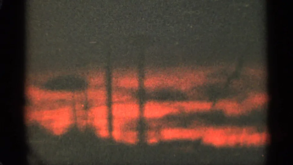 1965 Duluth 8mm frame with red sunset light diffused through clouds over a dark tree line.