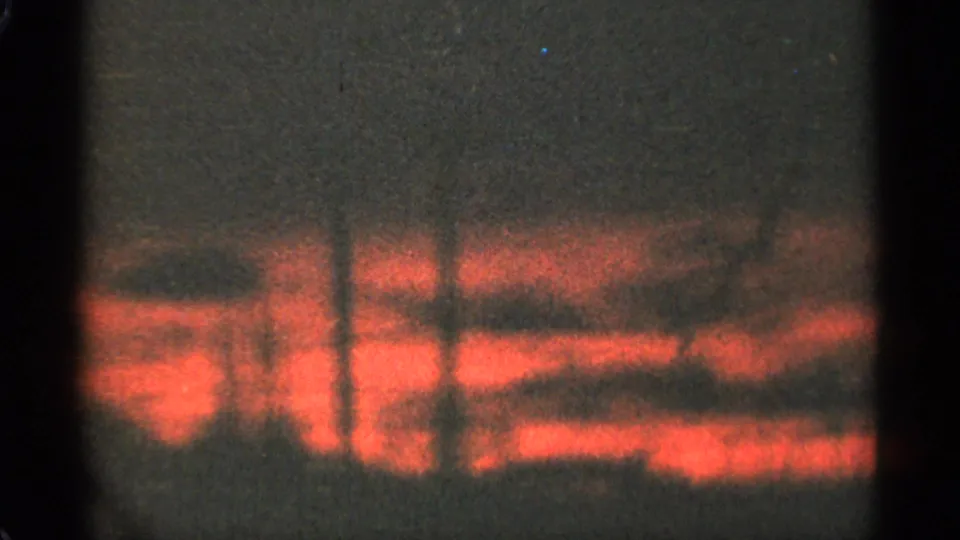 1965 Duluth 8mm frame with fading red sunset color, dark clouds, and a low silhouetted tree line.