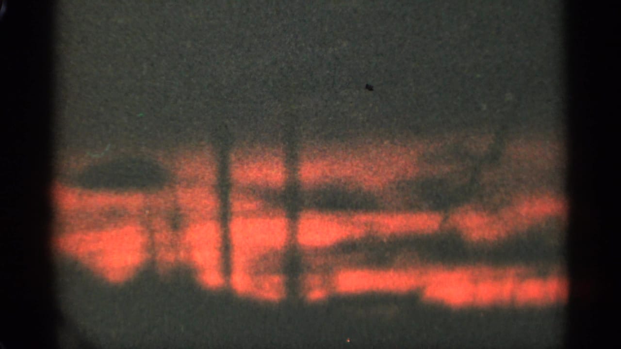 1965 Duluth 8mm frame showing glowing red-orange clouds near a dark horizon, with grain and black gate borders visible.