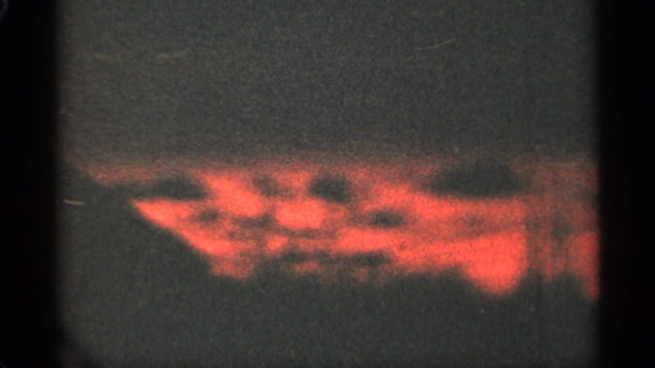 Soft red cloud shapes stretch across a darkening sky behind a film frame border.