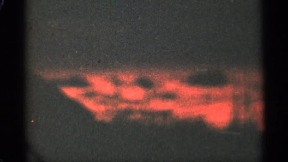 1965 Duluth 8mm sunset frame with red glowing clouds near the horizon, visible grain, speckles, and dark frame edges.