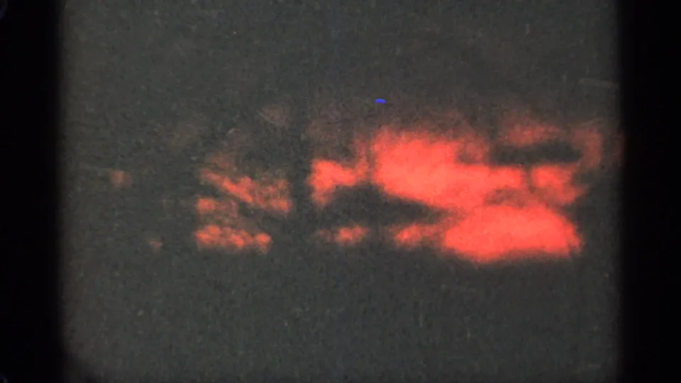 1965 Duluth home-movie frame with red-orange sunset light bleeding through dark wooded silhouettes.