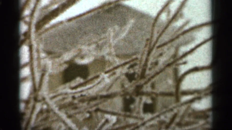A house exterior appears behind leafless branches in the 1965 Duluth winter home-movie frame.