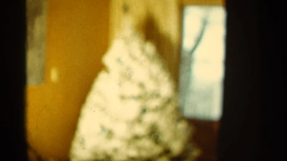 1965 home-movie still with the Christmas tree filling more of the frame while focus stays soft and warm-toned.