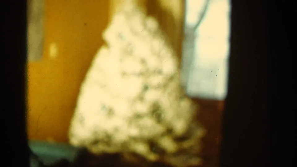 A warm, soft-focus 8mm view shows the same white cone-shaped form beside a bright window-like opening in a domestic interior.