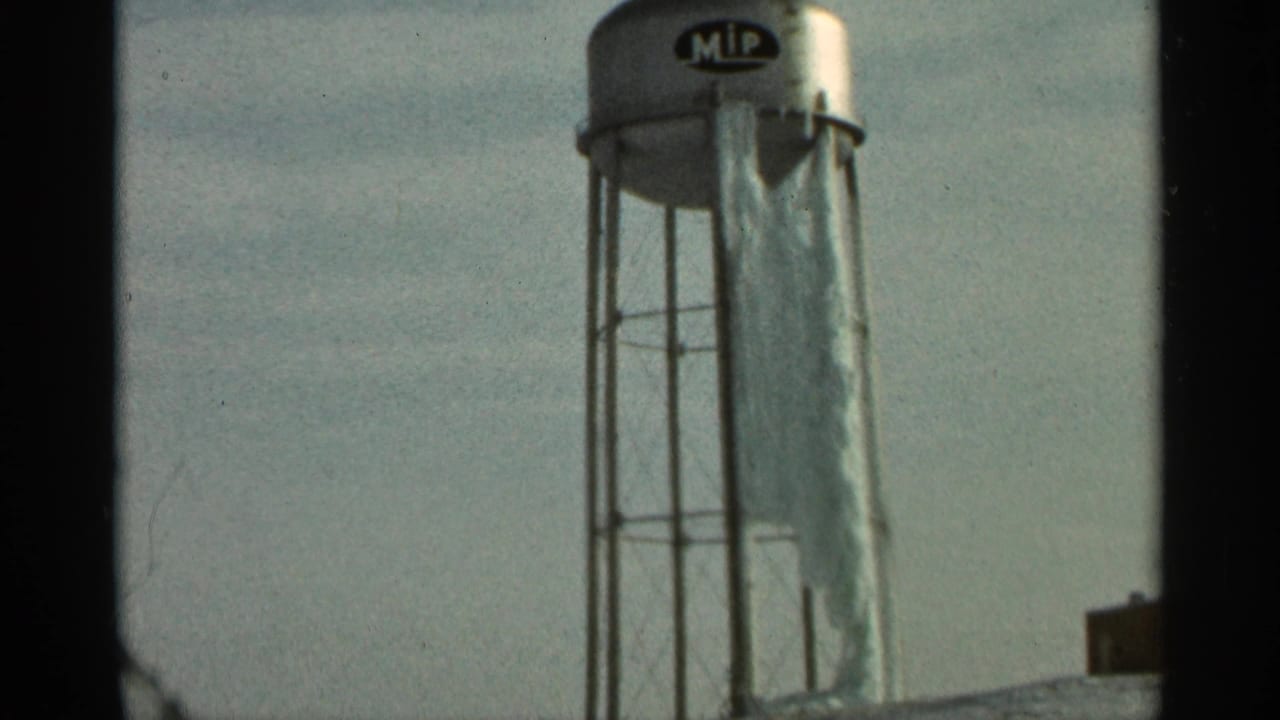 Silver MIP water tower with torn white tarp hanging from the side against a pale sky.
