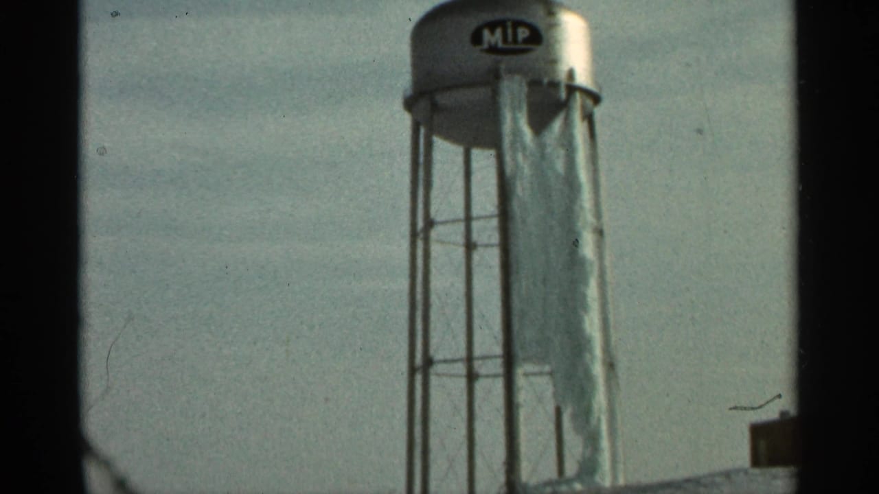 Water tower with MIP logo and hanging tarp, framed by dark film borders.