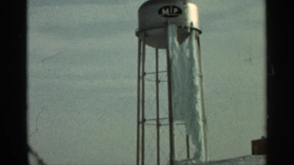1965 Duluth home-movie still showing the silver tower, support structure, and weathered tarp falling down the side.