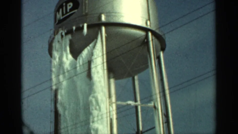 Closer 1965 Duluth view of the MIP-marked water tower, showing the underside, torn tarp, metal legs, and overhead wires.