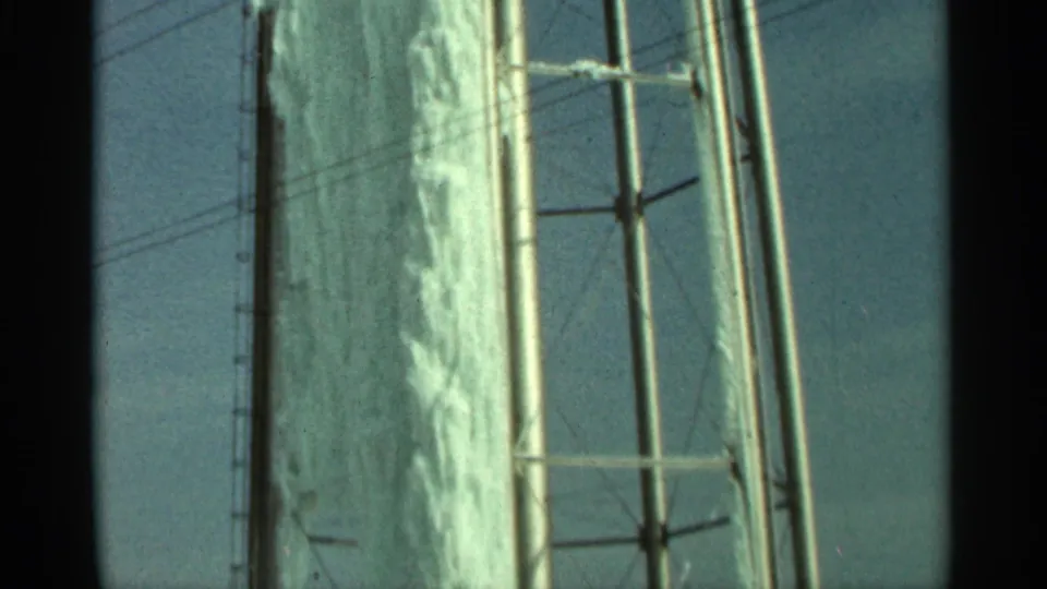 1965 Duluth home-movie frame showing dense ice on the side of a water tank, with braces and overhead lines visible nearby.