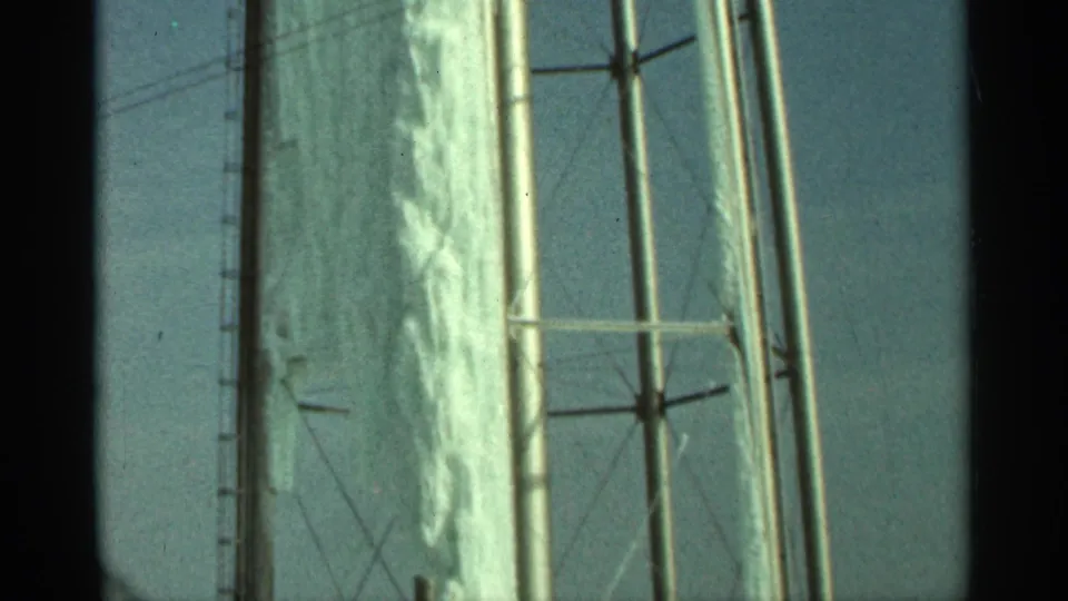1965 Duluth frame showing an iced tank surface beside tall steel supports, cross bracing, and power lines in the background.