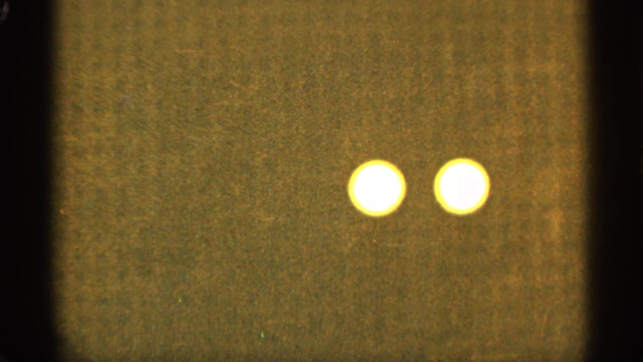 Two out-of-focus yellow-white light orbs appear near the upper center of an abstract 8mm frame associated with Duluth, Minnesota in 1965.