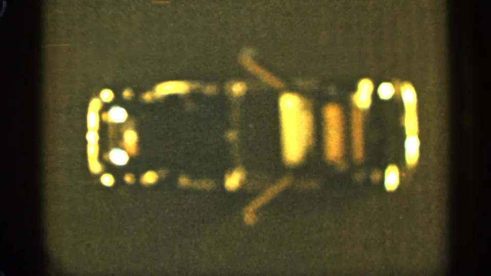 1965 8mm frame from Duluth showing a car-like light outline or toy display form against a dark background.