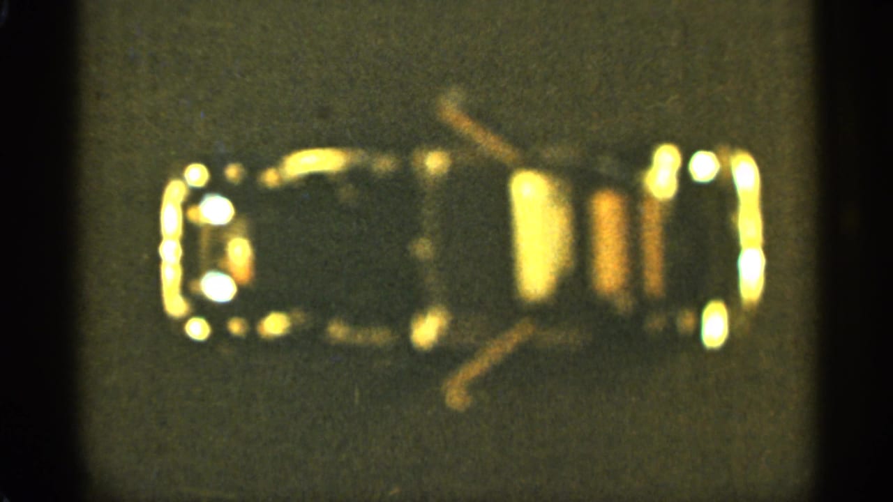 Small glossy object with bright yellow highlights centered on a dark gray background.