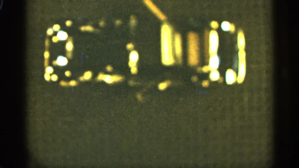 1965 home-movie still showing the same small dark object from above, with gold reflections softened by grain and motion blur.