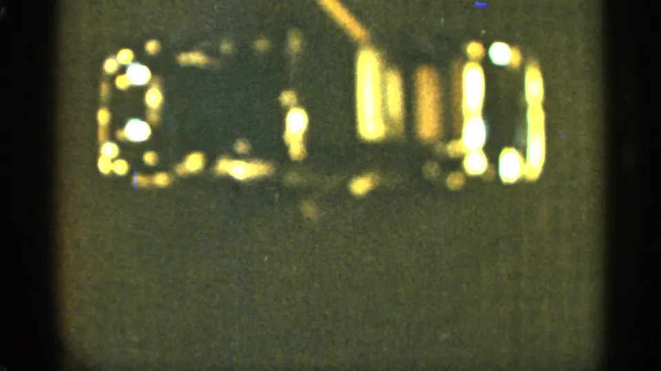 Duluth 1965 8mm frame with a top-down view of an indistinct small object, bright gold reflections, and dark film-frame edges.