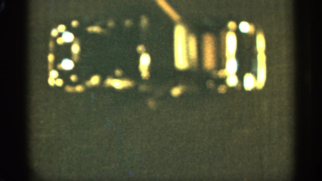 1965 Duluth 8mm frame showing a blurry reflective blue-and-gold toy car against a dark background.