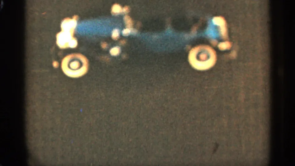 1965 Duluth 8mm frame showing the blue toy car in profile with pale wheels on a dark textured background.