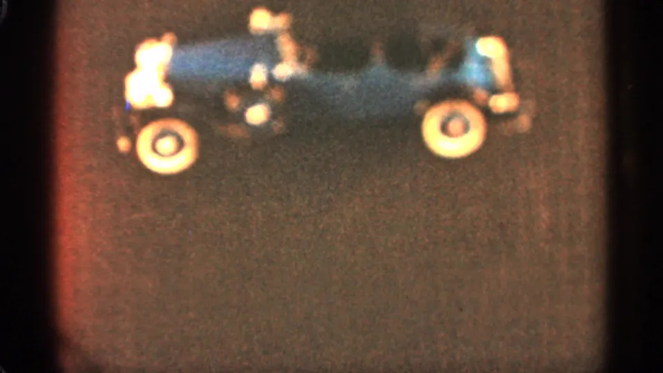1965 Duluth home-movie frame showing the stationary blue toy car with warm color shift and soft 8mm texture.