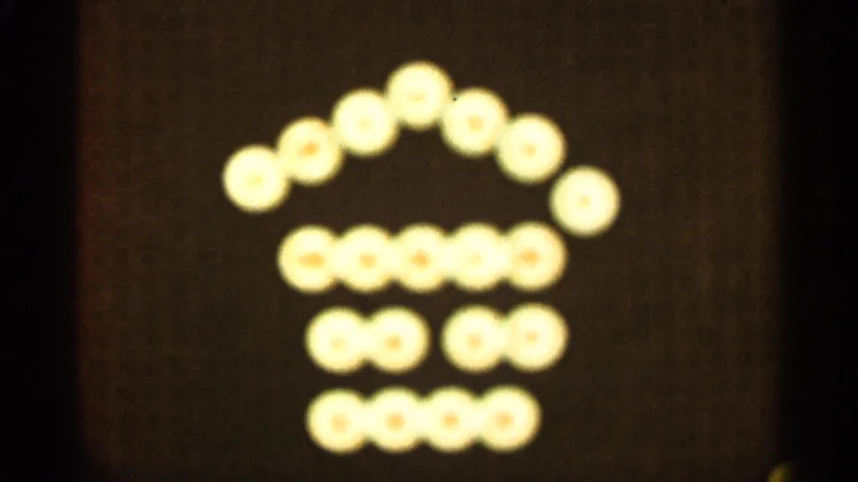 In this 1965 Duluth 8mm frame, rows of soft glowing lights appear arranged as a simple house shape on a dark background.