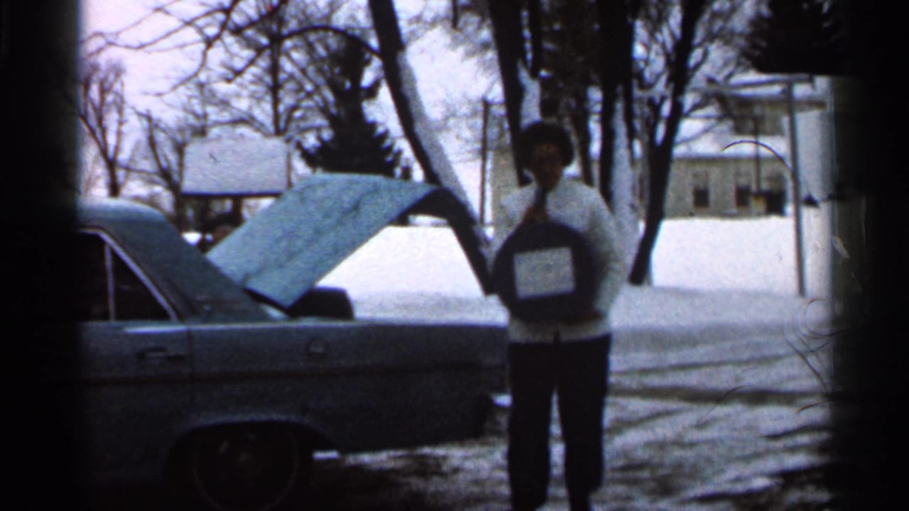 Woman carries a round dark object away from the open trunk in snow.