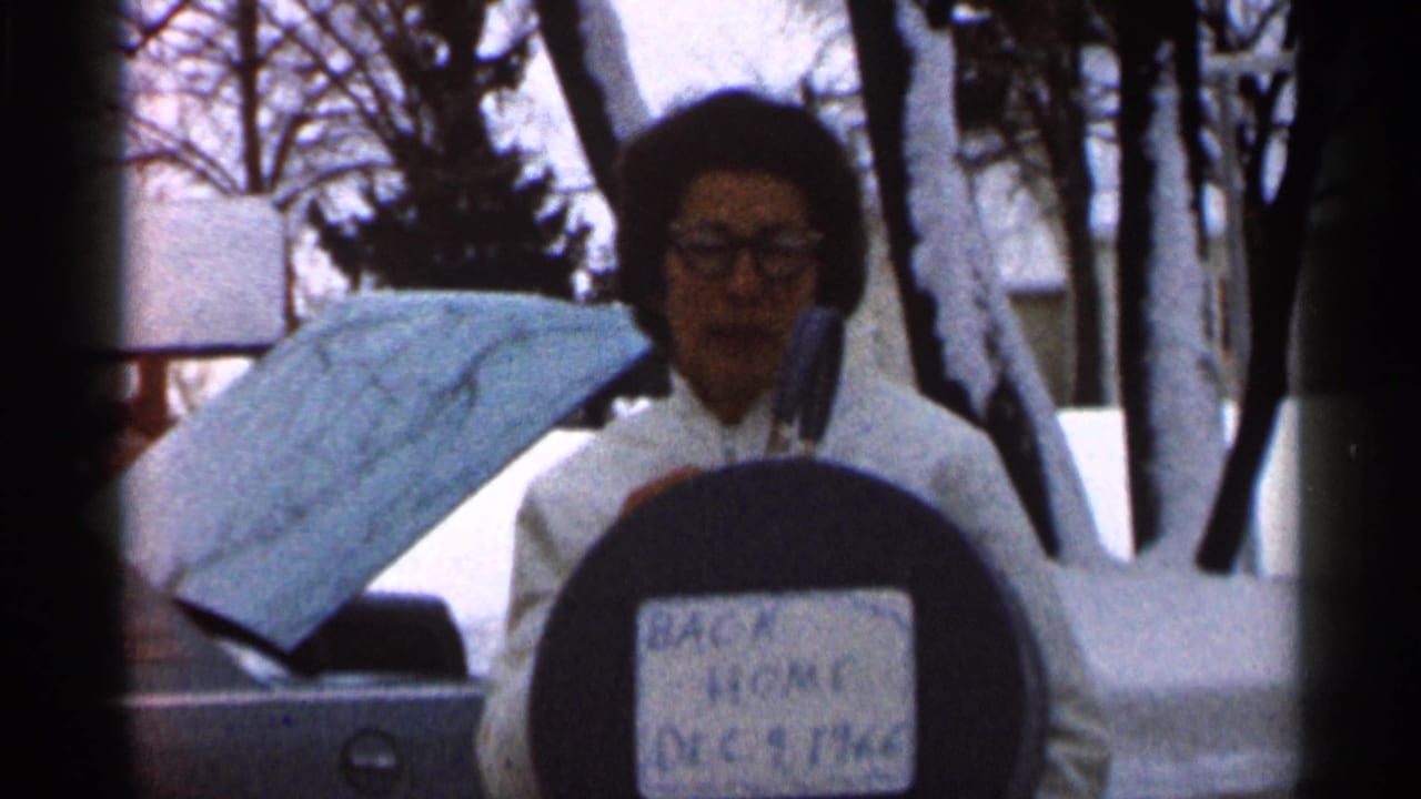 In Eau Claire, Wisconsin, a woman in glasses and a white winter coat poses in snow with a label reading “BACK HOME DEC 9 1966.”