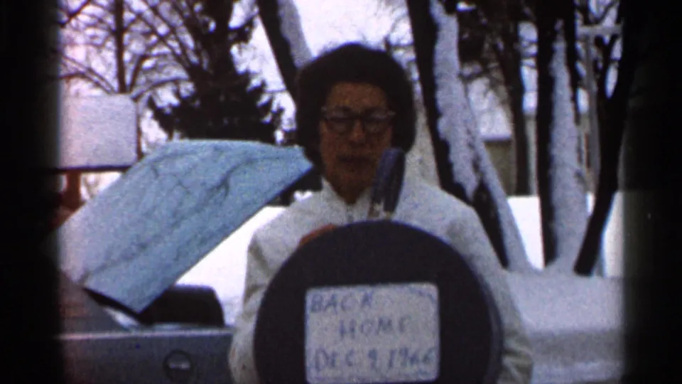 In Eau Claire, Wisconsin, a woman in glasses and a white winter coat poses in snow with a label reading “BACK HOME DEC 9 1966.”
