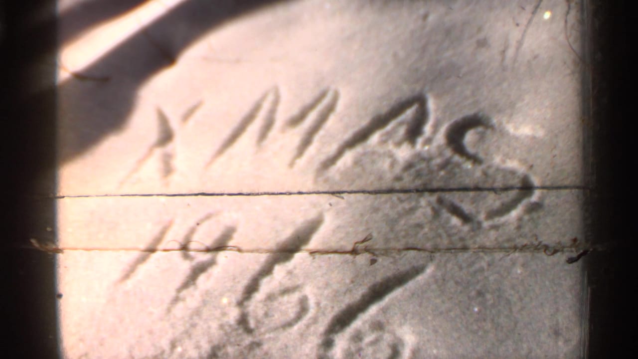 Close view of letters and numbers scratched into snow, partly obscured by film damage.