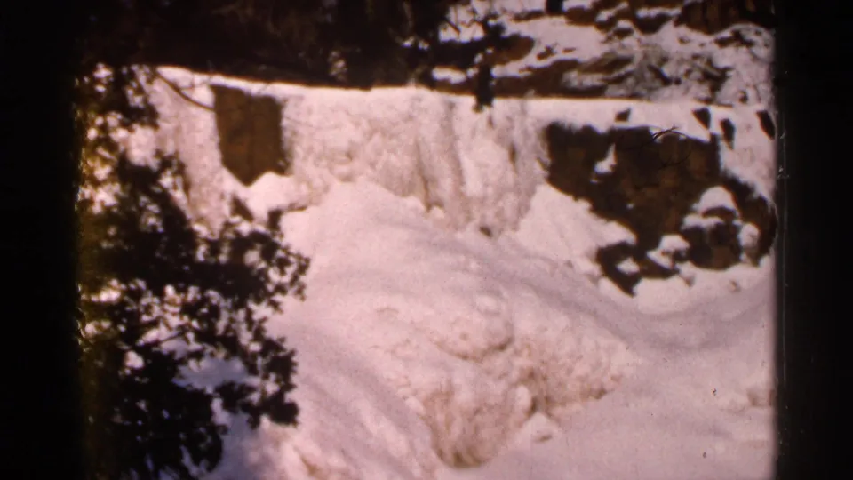 A bright 1966 winter snow mound framed by trees and rocks in the Eau Claire home-movie footage.