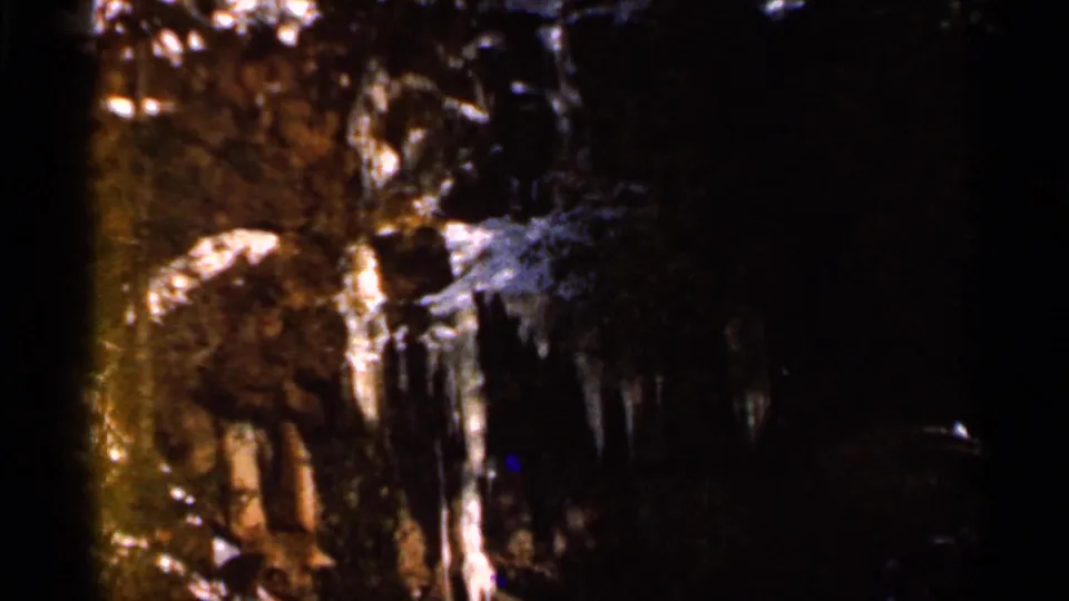 1966 Eau Claire home-movie frame showing dark snow-covered trees and icicles with heavy 8mm edge shadow.