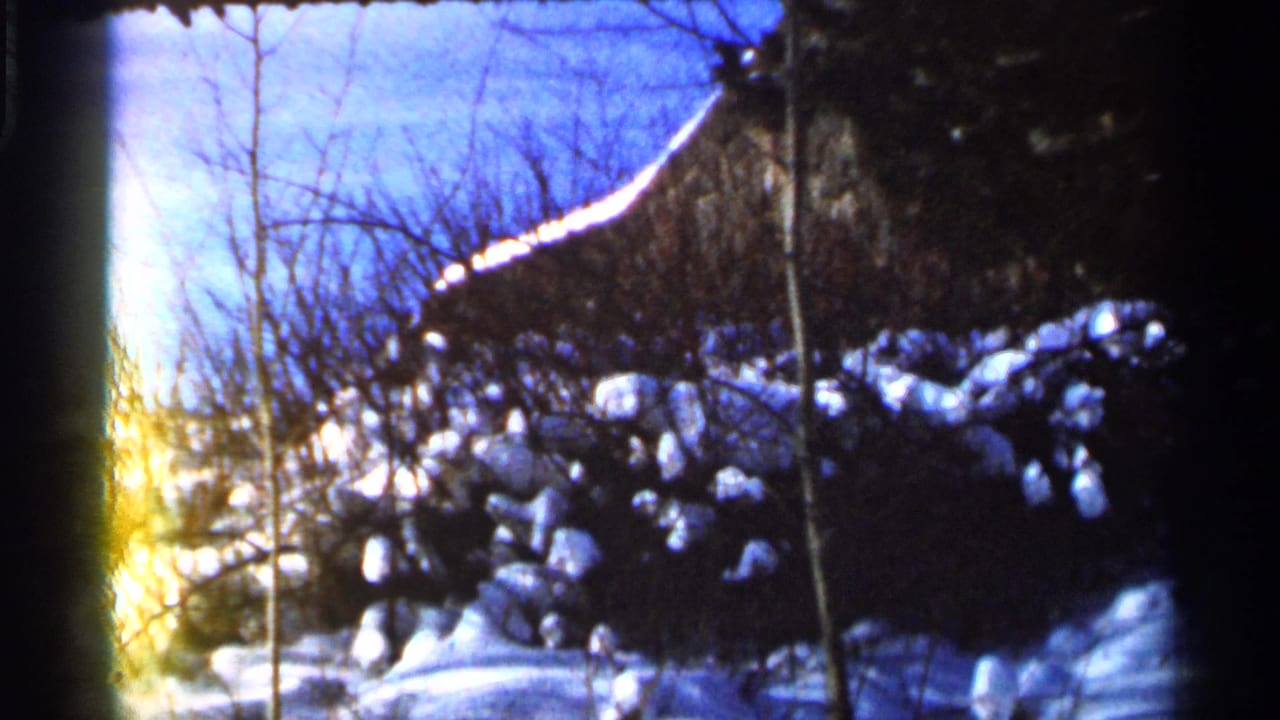 Snowy trees and ground beside a dark structure, framed by 8mm film edges.