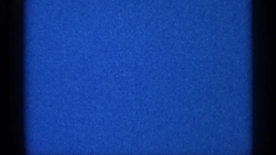 End frame showing blue leader or blank 8mm film with visible grain, specks, and edge shading.