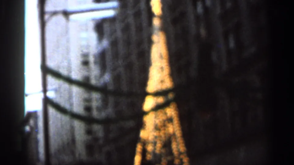 1966 Florida home-movie frame with a bright tower-like replica viewed through dark framing and streaked glass at night.