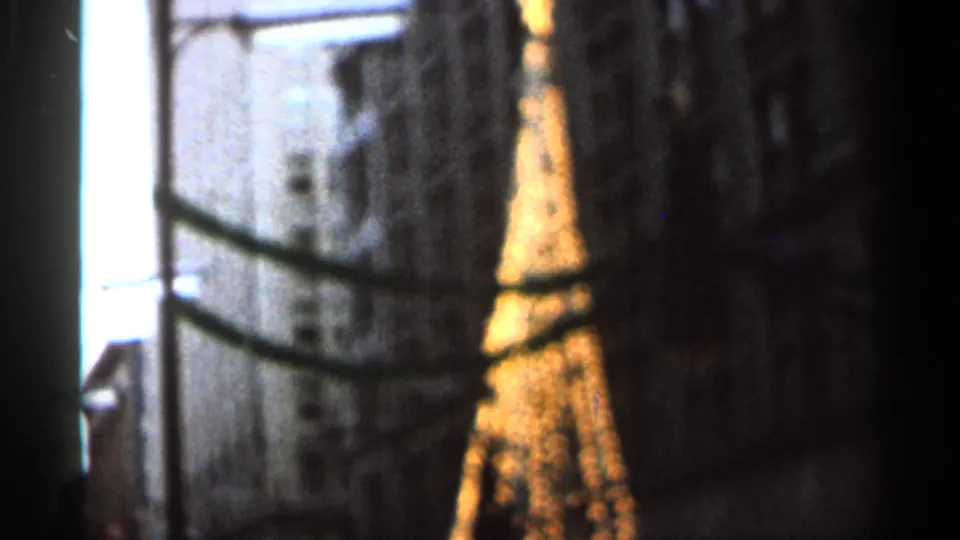 Soft 8mm nighttime view of an illuminated Eiffel Tower-like replica in Florida, partly obscured by dark foreground framing.