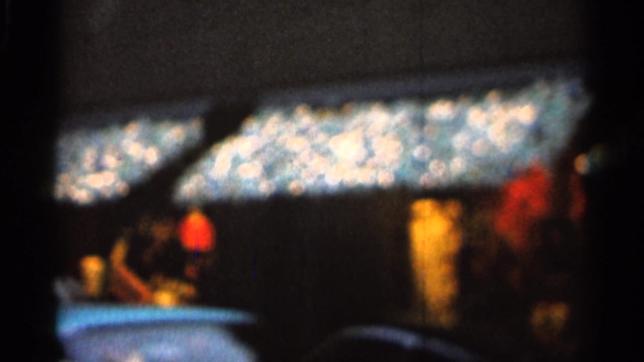 Blurred night street view with bright storefront lights, pedestrians, and parked cars.