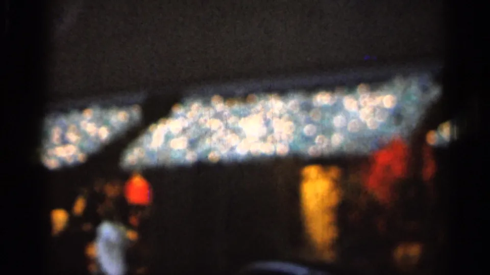 1966 Florida home-movie frame with glowing storefront lights, red and yellow bokeh, and blurred pedestrians on a dark street.