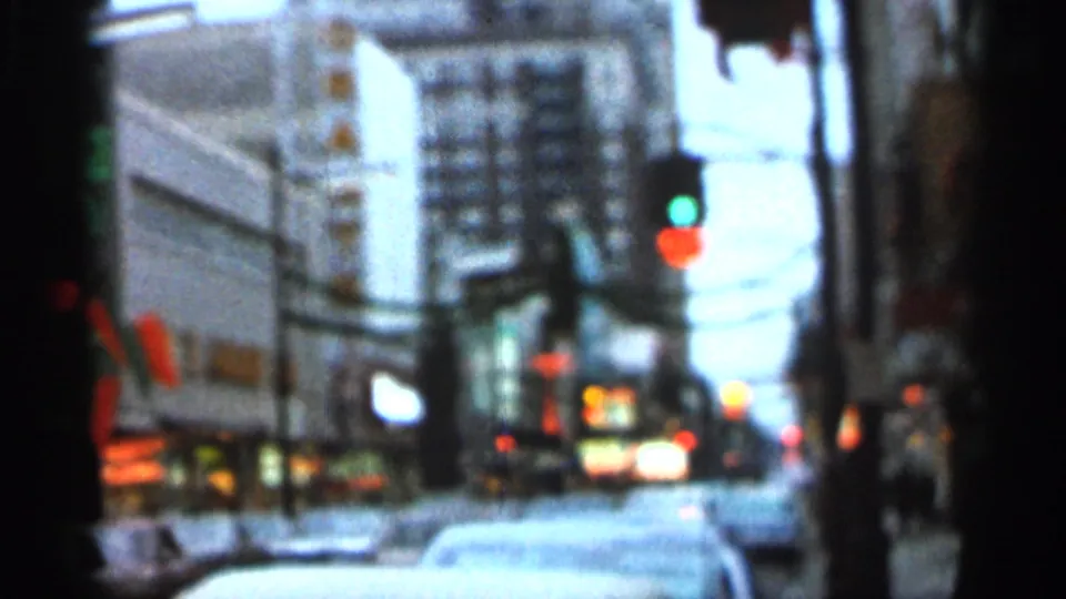 Soft 8mm frame from the Florida clip showing a street corridor, traffic signal lights, building facades, and cars in heavy blur.