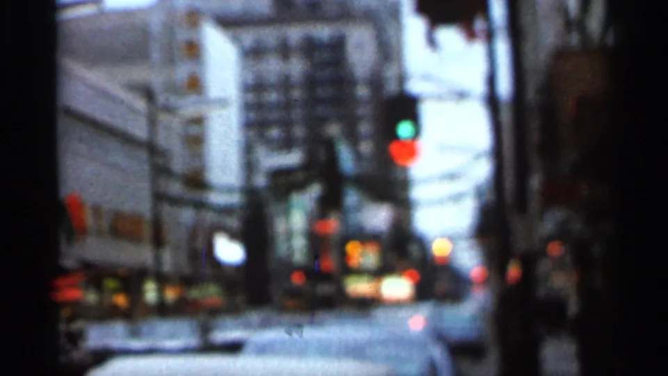Soft-focus 1966 Florida street frame with red and green signal lights, blurred buildings, vehicles, and dark film-frame edges.