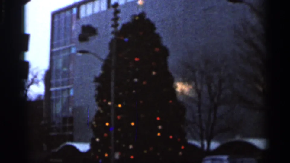 1966 Florida 8mm frame with a softly exposed Christmas tree, colored lights, streetlight, and modern building in an urban setting.