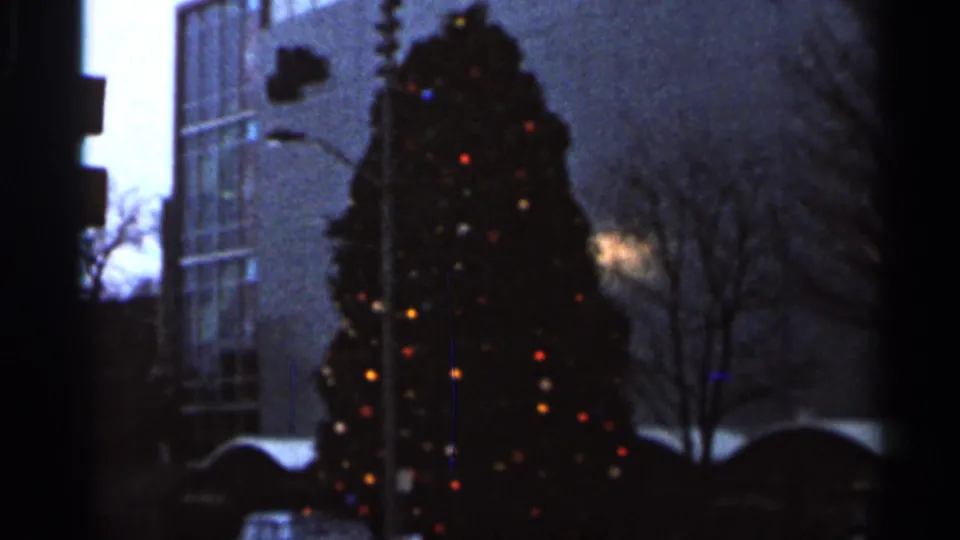 1966 Florida 8mm frame showing the holiday tree still in view, with colored lights, a streetlight, and urban building backdrop.