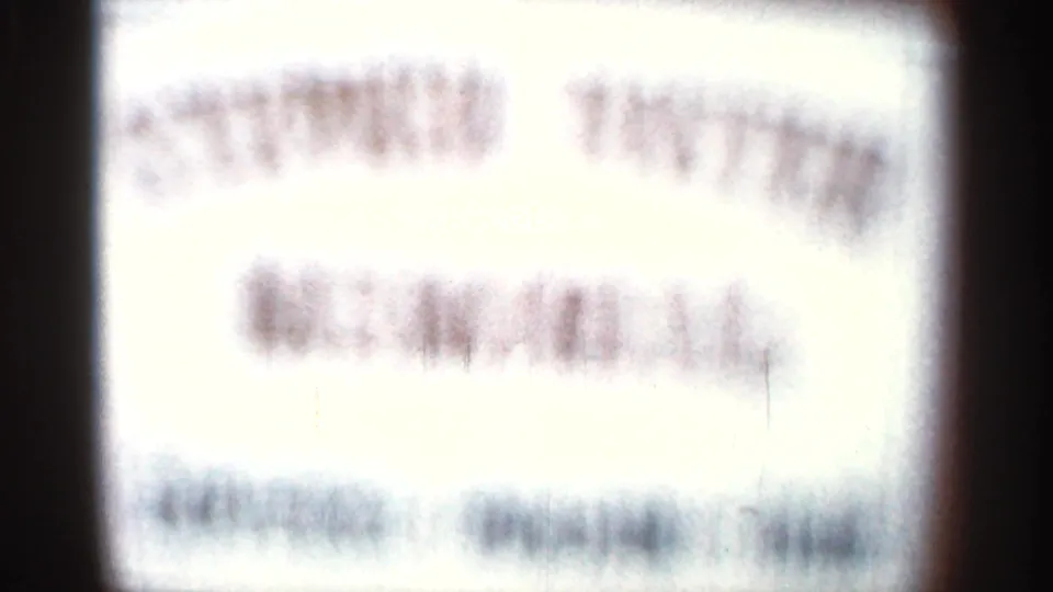 Out-of-focus 8mm close-up of a bright sign, with blurred lines of lettering that cannot be read.
