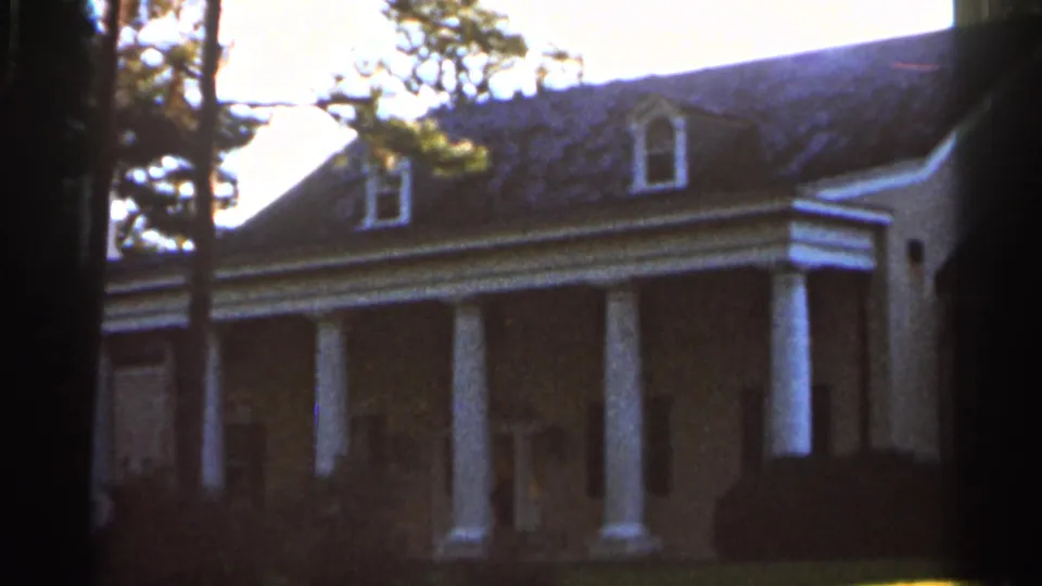 1966 Florida home-movie frame showing a weatherboard house with white porch columns, dormers, trees, and shrubs.