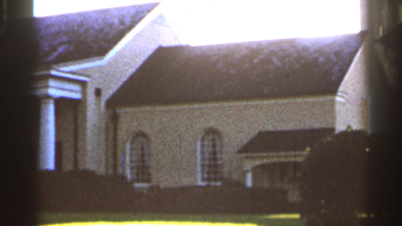 1966 Florida 8mm frame showing a large white exterior with columns, arched windows, dark roof, lawn, and shrubs.