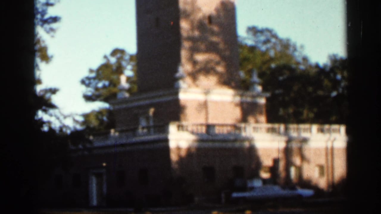 1966 Florida 8mm frame showing a white-and-brick tower seen from ground level, partly framed by trees and deep shadow.