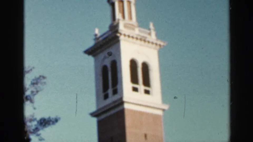 1966 Florida 8mm frame focused on the tower's white upper level, arched openings, and cupola against blue sky.
