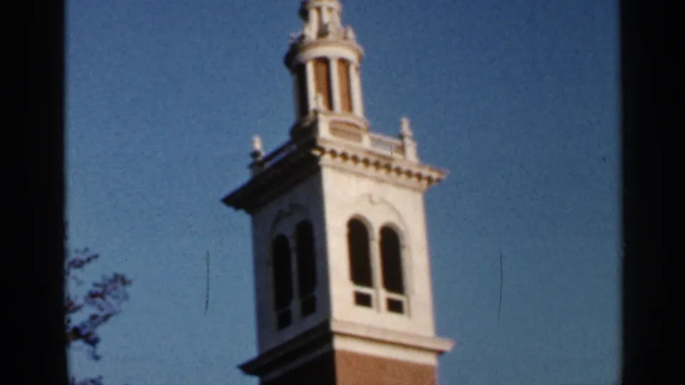 1966 Florida 8mm frame of the tower's upper stories, showing white architectural detail, brickwork, cupola, and blue sky.