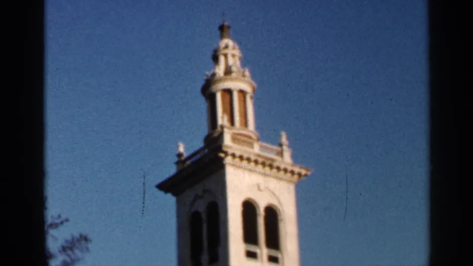 1966 Florida 8mm frame of a white tower or cupola with arched openings, blue sky, and visible film edges.