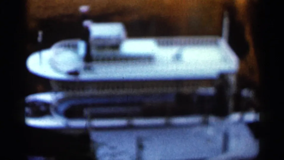 1966 Florida 8mm frame showing a white miniature ocean-liner-style ship model with decks and railings indoors.