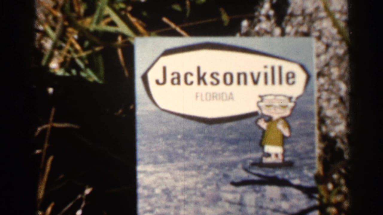 Jacksonville Florida sign with a small cartoon mascot near grass and tree bark.